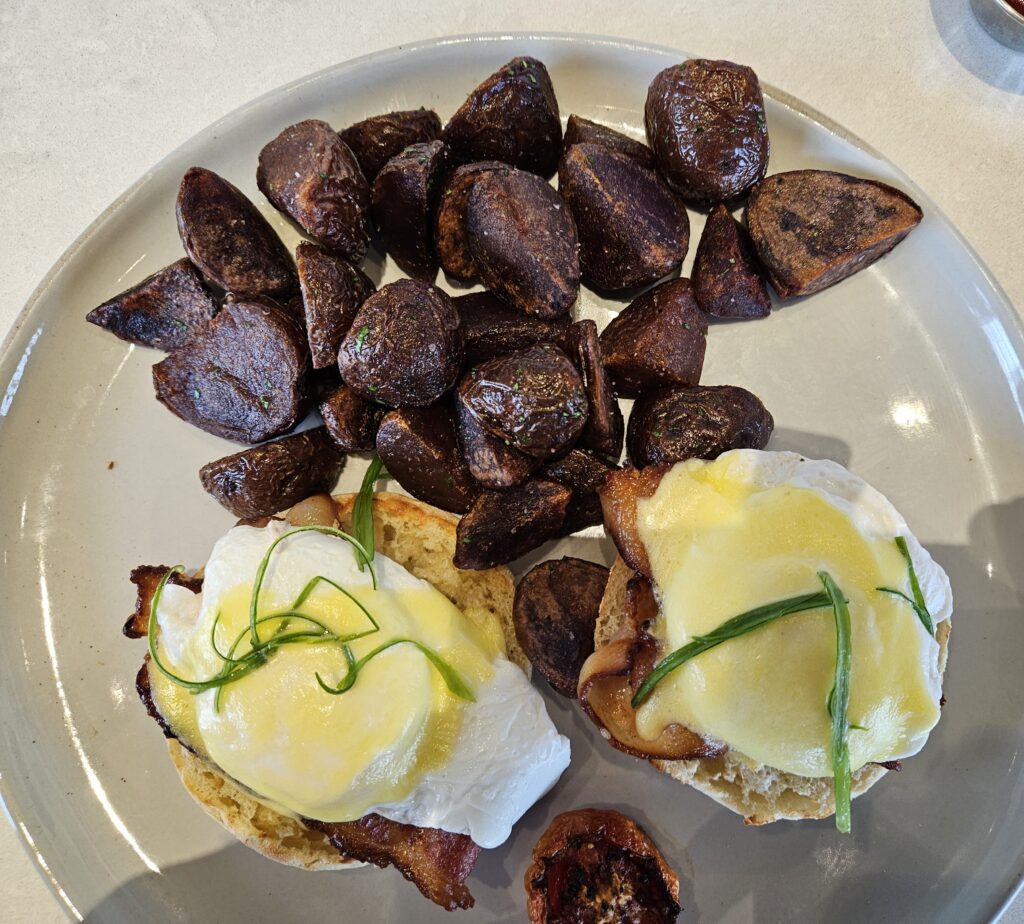 Eggs benedict. 2 poached eggs with hollandaise sauce. Purple potatoes.