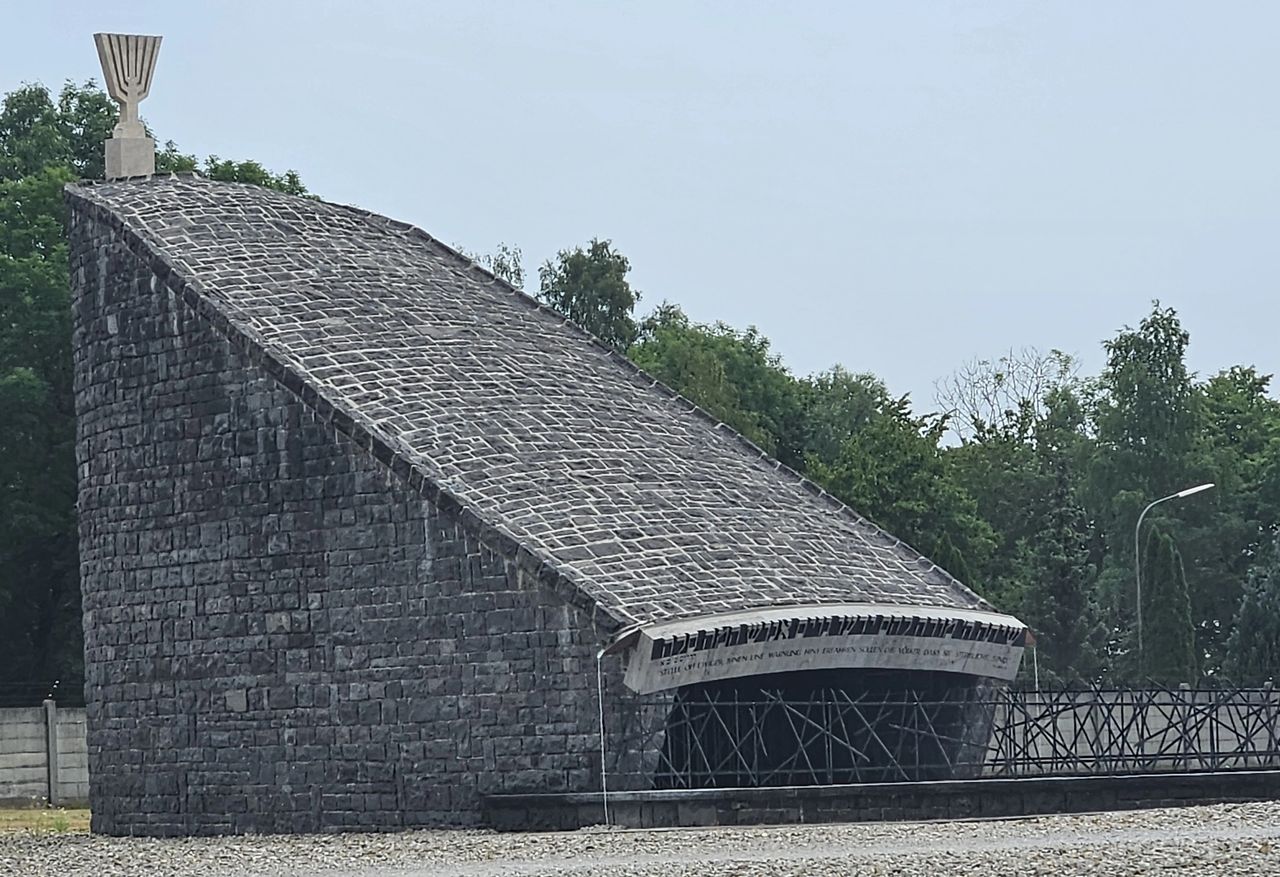 The Jewish memorial at Dachau. Dark grey stone structure with a steeply slanted roof. Menorah on top.