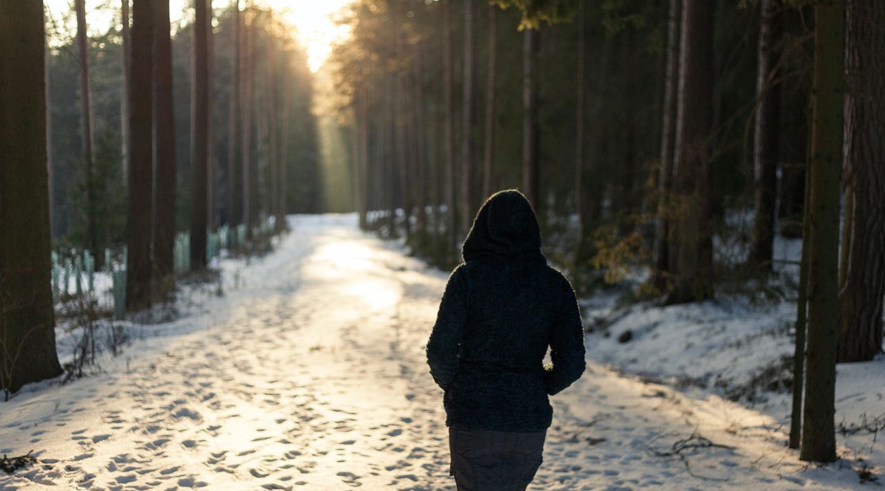 A woman walks down a quiet country, snow covered road.