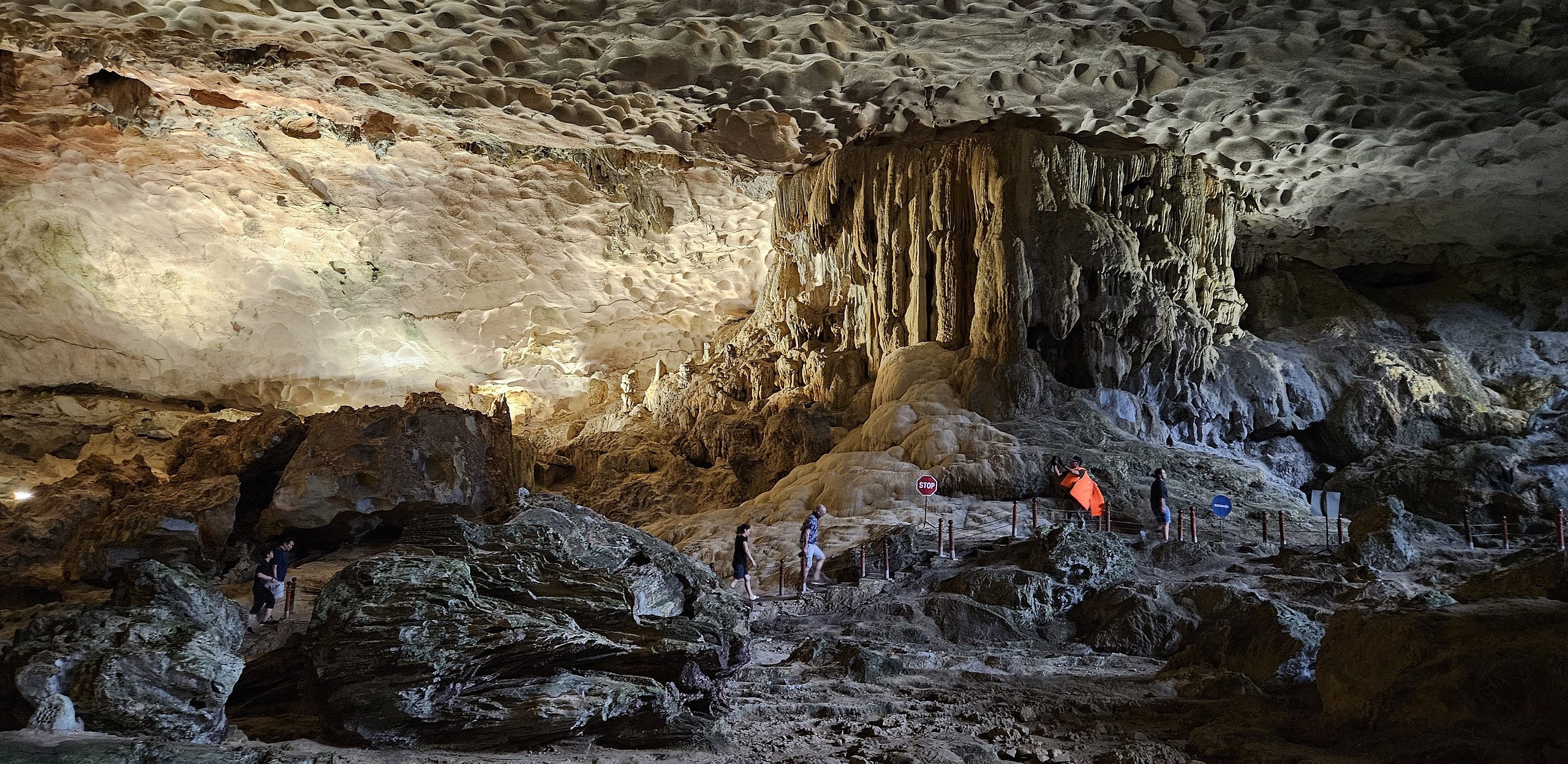 A massive stalactite joins the floor and ceiling on a massive cave. A walking path has a few people to show size