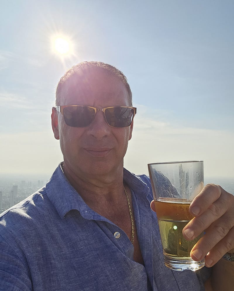 Cheers from the roof! A man sips a beer with the blue sky and distant Bangkok skyline.