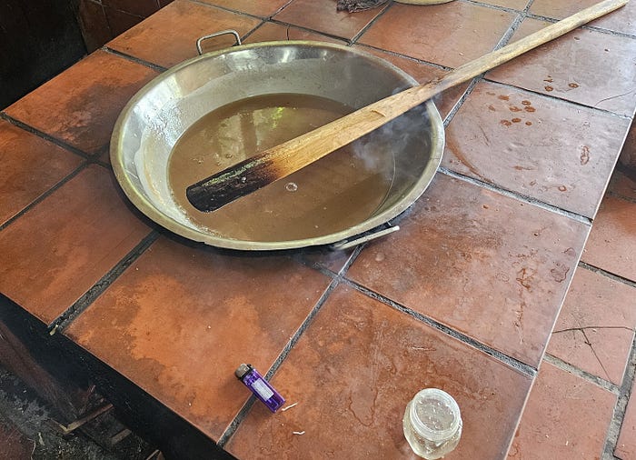 A bowl of thick brown coconut candy liquid sits on a table with a long stir stick.