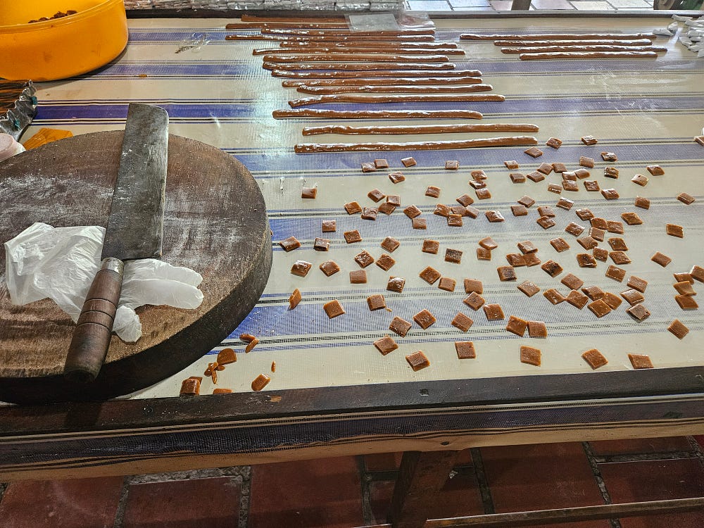 Cooled half-inch strips of candy are cut into squares. A massive cleaver sits on the cutting board.