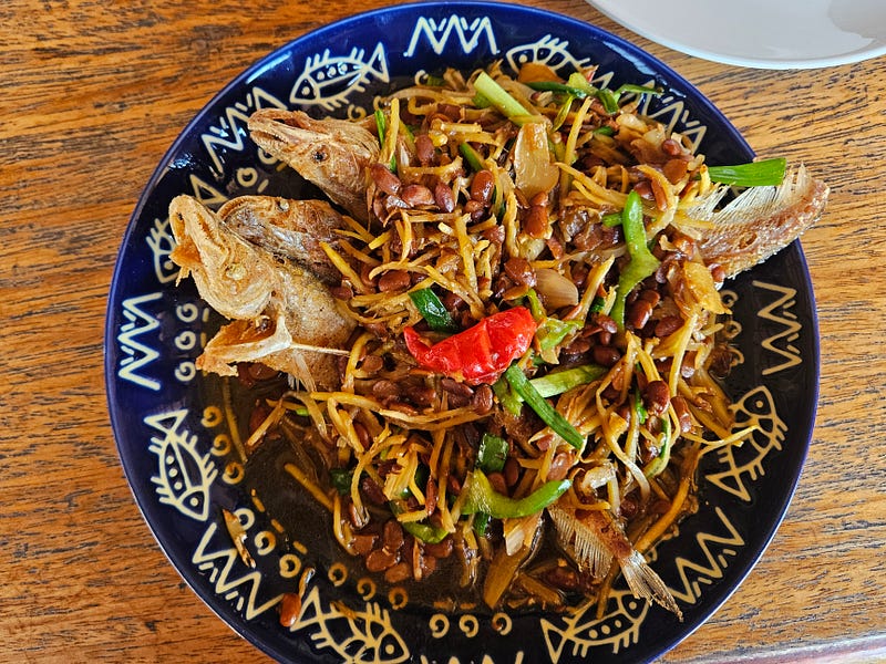 A Cambodian dish. 3 knifefish on a plate covered in noodles and bean sauce