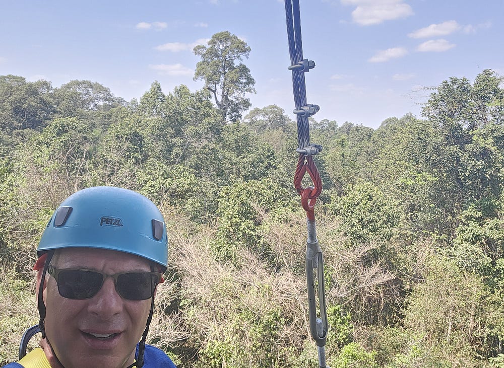 The head of a man in a funky blue helmet stands against a backdrop of the Cambodian forest.