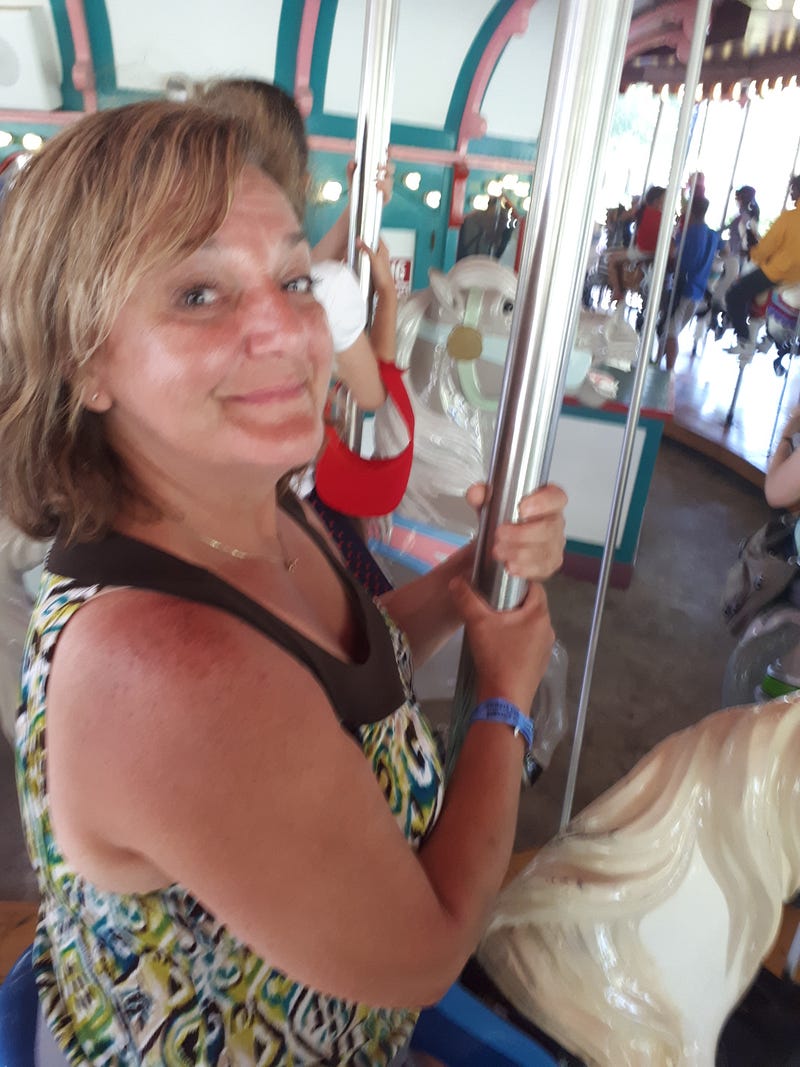 A woman, my wife sits on a carousel at a theme park.