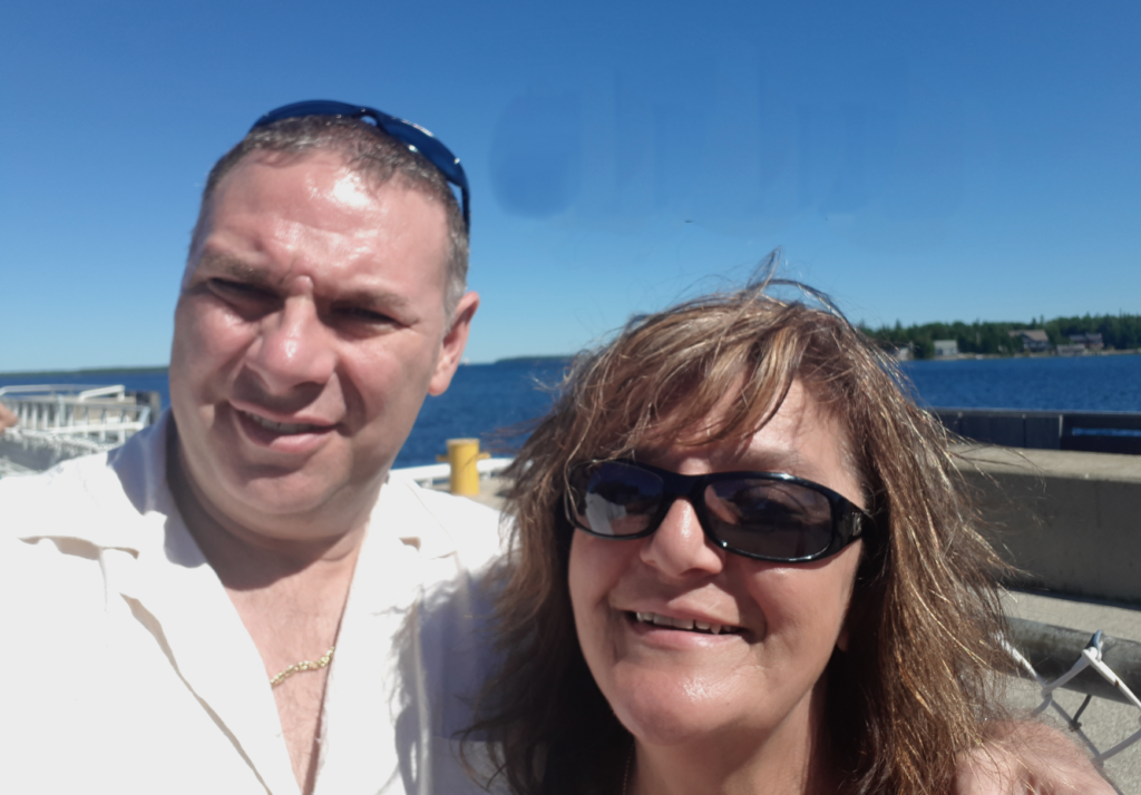 A man and woman smile for the camera. Lake water behind them.