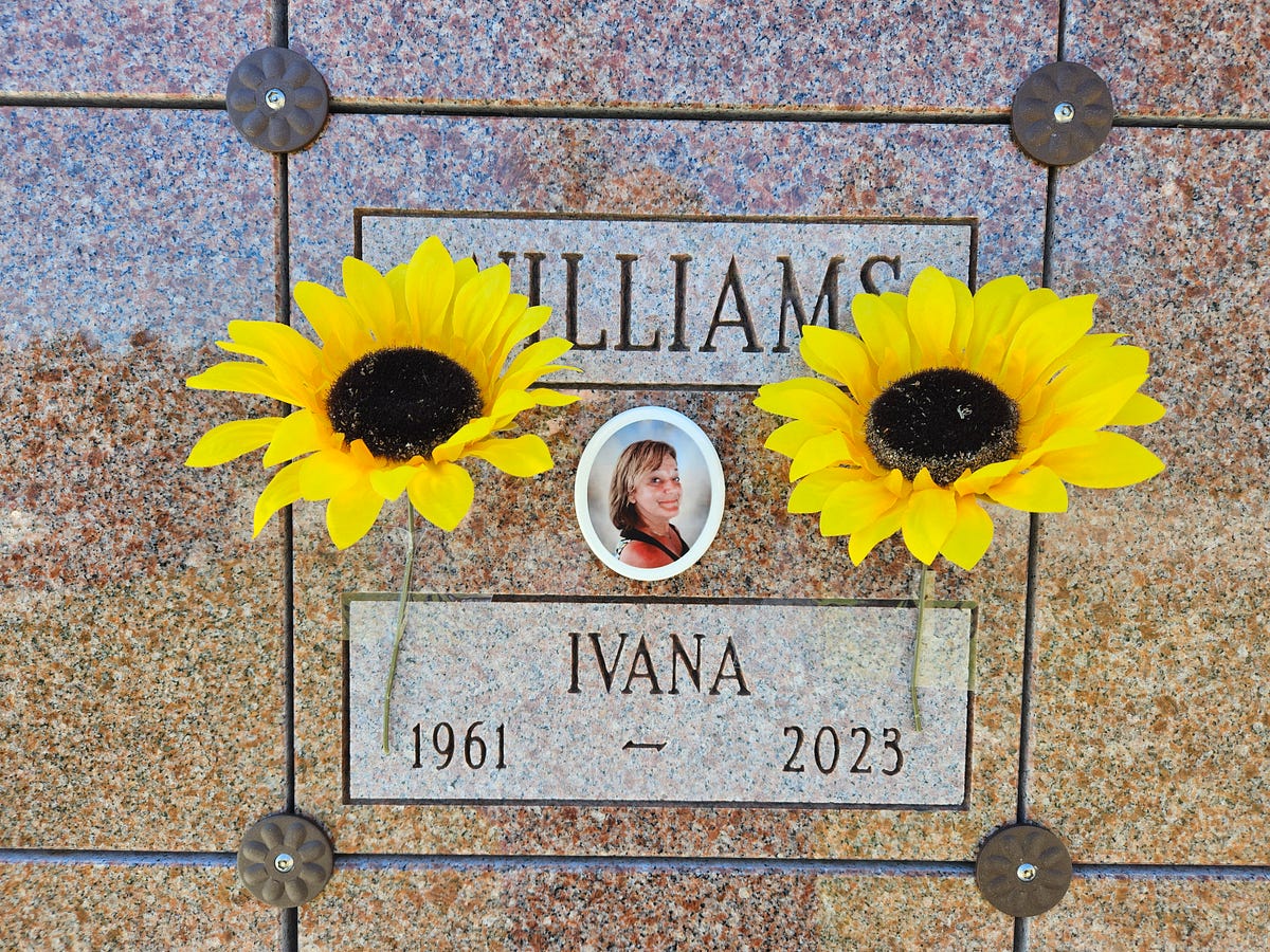 The  marble front of my wife’s columbarium. Her picture in the middle, flanked by plastic sunflowers.